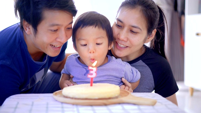 男孩和父母一起吹生日蜡烛。视频素材