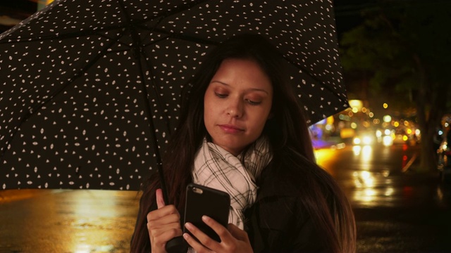 一个女人在雨伞下微笑着用智能手机发短信视频素材