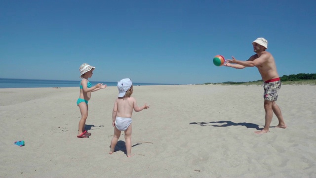 一位美国父亲喜欢和孩子们在沙滩上玩球。家庭夏日海滩度假。缓慢的运动。视频素材