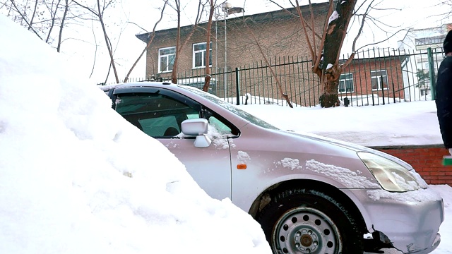 一名男子在居住区用刷子清理汽车上的积雪。视频素材