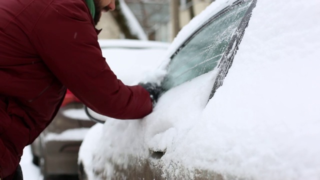 一名男子在住宅区用手清理汽车上的积雪视频素材