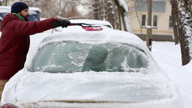 一名男子在居住区用刷子清理汽车上的积雪视频素材