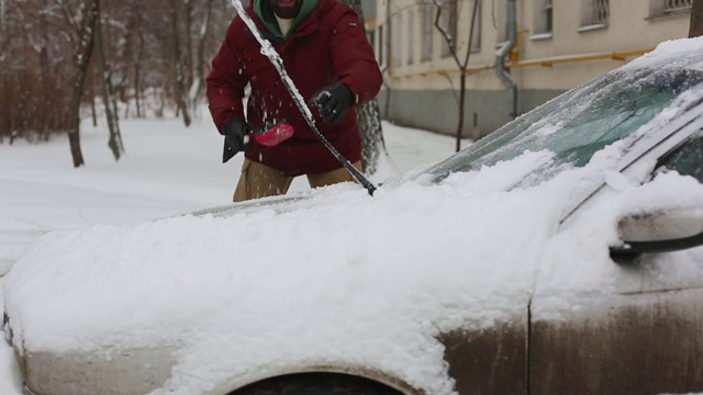 一名男子在居住区用刷子清理汽车上的积雪视频素材