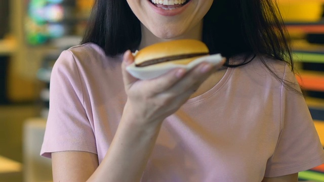 微笑的女人在镜头前展示美味和风味的汉堡，肥胖的风险视频素材