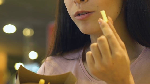 年轻女子喜欢吃咸脆的薯条，油腻的零食视频素材