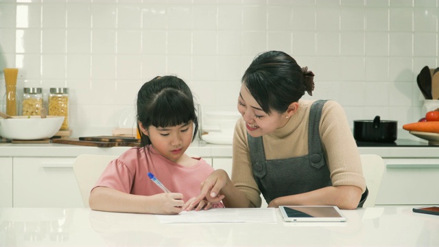 妈妈在现代厨房里用平板电脑教女儿做作业视频素材