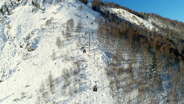 高山滑雪胜地树林中滑雪缆车的鸟瞰图。在雪山滑雪缆车的飞行视图。冬季滑雪和单板滑雪的好天气。视频素材