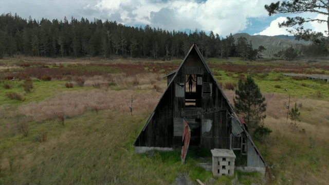 航拍:草地上破败小屋窗户上年轻女子的剪影视频素材