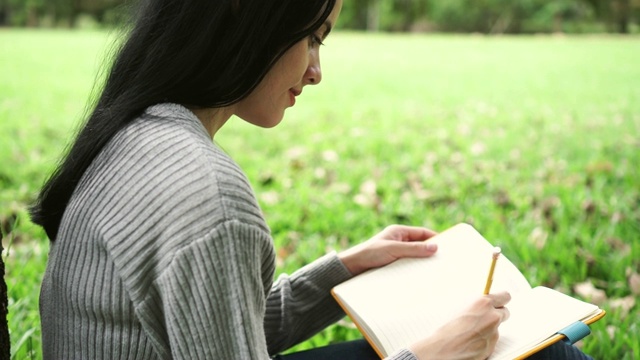 年轻有吸引力的女人有一个新的想法和写在笔记本上在公共公园视频素材