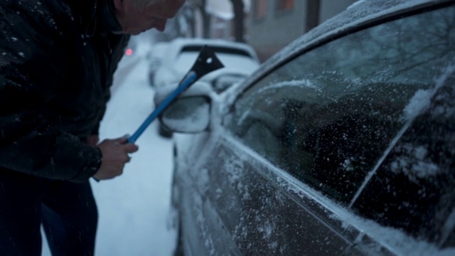 一位老人正在清除车上的霜雪视频素材