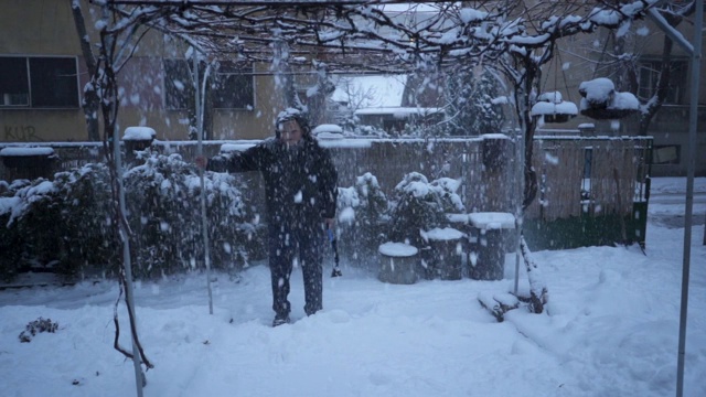 一位老人在后院抖落葡萄架上的雪视频素材