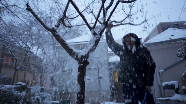 老人在前院摇晃树枝上的雪视频素材