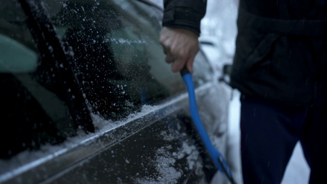 一位老人在城市街道上清理车上的积雪视频素材