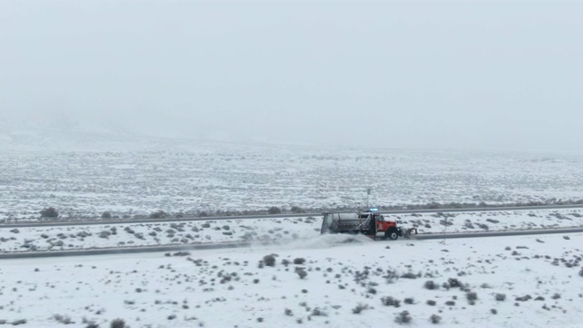 无人机拍摄的扫雪机沿着高速公路通过一个多雪的，岩石沙漠景观在一个阴天的冬天视频素材