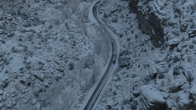 高空无人机拍摄的一辆汽车在一条道路上行驶在一个下雪的岩石悬崖在沙漠景观在冬天视频素材