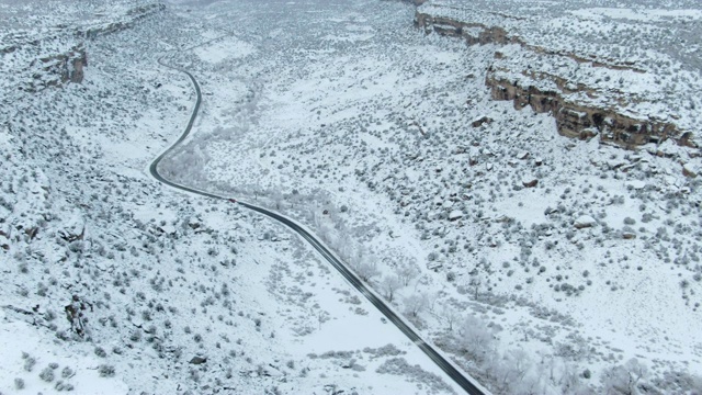 高空无人机拍摄的一辆汽车在一条道路上行驶在一个下雪的岩石悬崖在沙漠景观在冬天视频素材