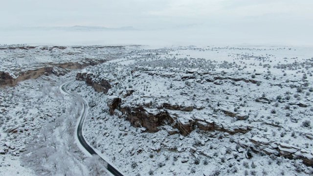 头顶无人机拍摄的道路蜿蜒通过一个下雪的，多岩石的沙漠景观在冬天阴天下视频素材