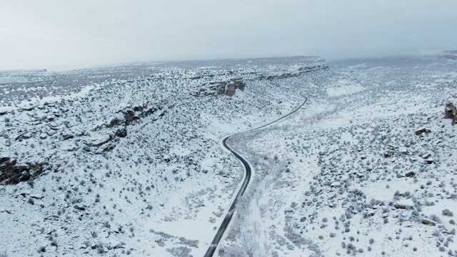 头顶无人机拍摄的道路蜿蜒通过一个下雪的，多岩石的沙漠景观在冬天阴天下视频素材