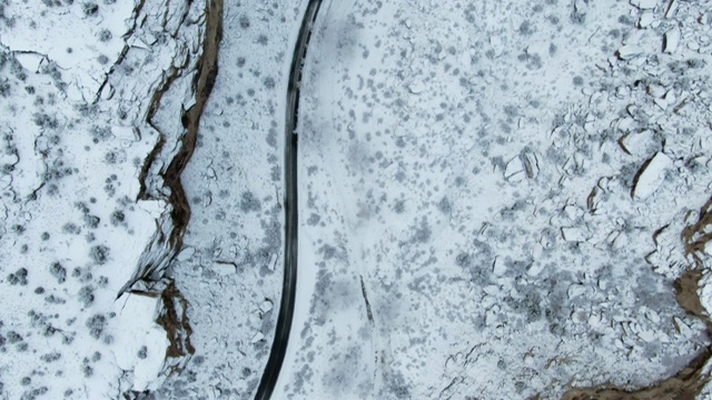 无人机拍摄的冬日里一条蜿蜒穿过岩石沙漠峡谷的雪道视频素材