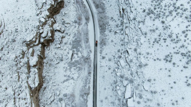 直接头顶无人机拍摄的雪犁驾驶在道路旁边的一个多雪，岩石悬崖在沙漠景观在冬天视频素材