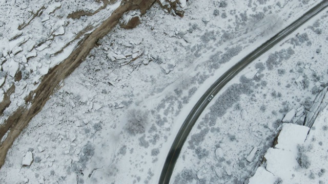 直接头顶无人机拍摄的一辆汽车在一个冰雪沙漠景观的道路上行驶在岩石峡谷旁边的冬季视频素材