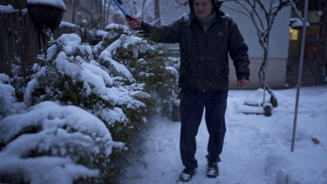 一位老人正在清除前院植物上的积雪视频素材