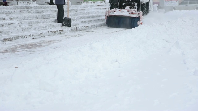 一辆带有大刷子的拖拉机正在清扫城市街道上的积雪。视频素材