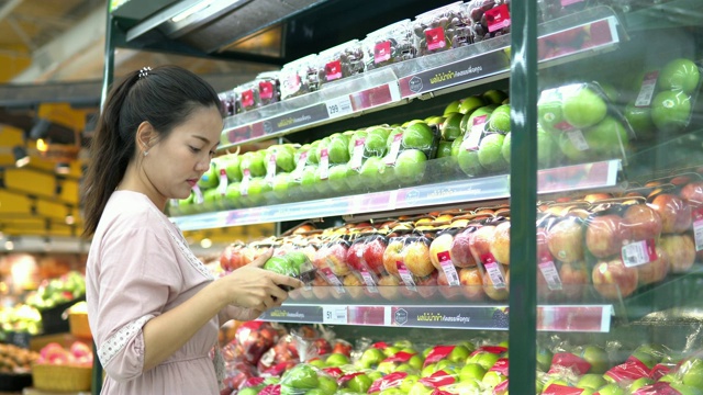 年轻女子在超市选择了水果和购物视频素材