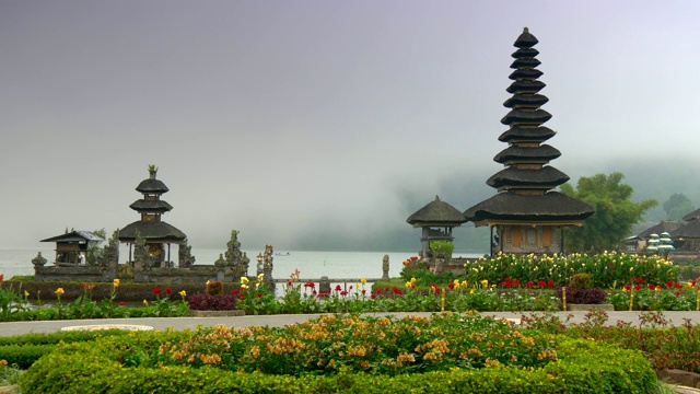 印尼巴厘岛。Pura Ulun Danu Bratan Temple四周环绕着美丽的花朵，背景是薄雾覆盖的水。Pura Bratan是湿婆崇拜的水神庙。4 k视频素材