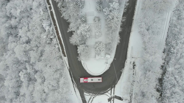 鸟瞰图转向公路在山区冬季积雪覆盖森林视频素材