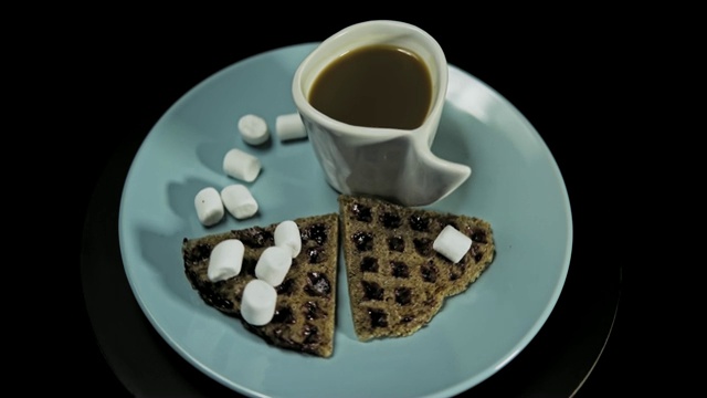 蓝色盘子上的黑心华夫饼，黑色背景上的咖啡杯。视频素材