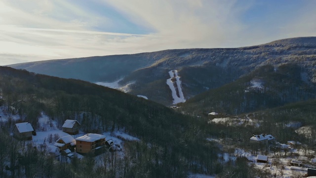 冬天的山区乡村景观。白雪覆盖的房屋在大雪中飞过了山峦和村庄。视频素材