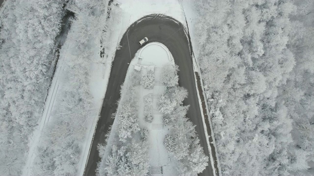 鸟瞰图转向公路在山区冬季积雪覆盖森林视频素材