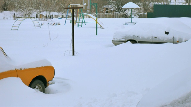 汽车被雪覆盖，在严冬的暴风雪中。车在院子里下着雪。视频素材