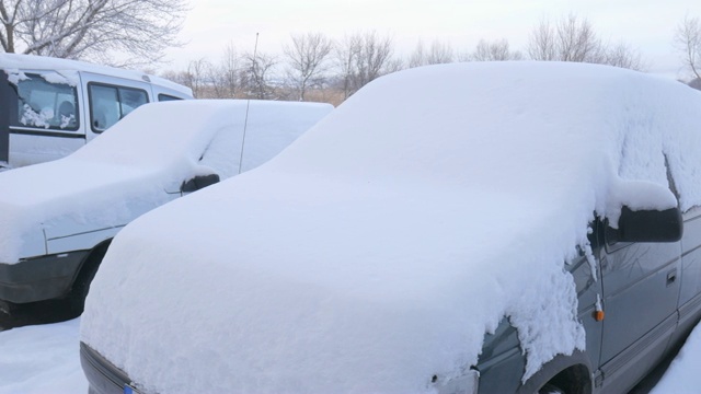 汽车被雪覆盖，在严冬的暴风雪中。车在院子里下着雪。视频素材