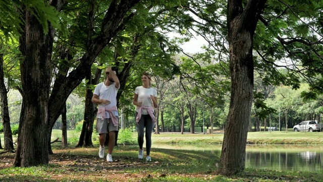 一对年轻夫妇在一个阳光明媚的日子里在公园里慢跑和跑步。健康生活，生活方式理念。慢动作视频素材