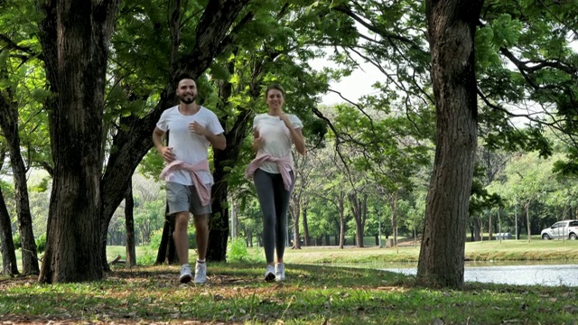 年轻夫妇慢跑和跑步。在一个阳光明媚的日子里，在公园户外庆祝击掌快乐的姿势。健康生活，生活方式理念。慢动作视频素材