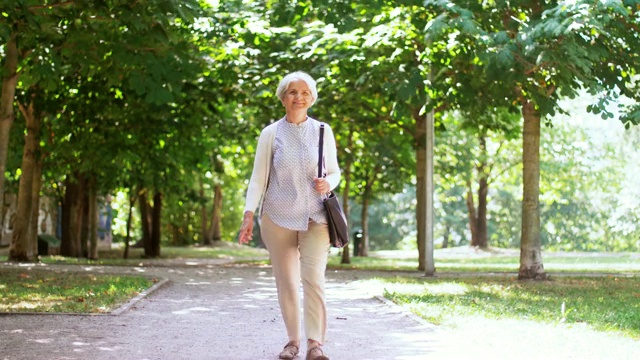 快乐的老年妇女沿着夏季公园散步视频素材