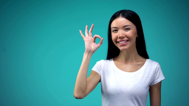 乐观的亚洲妇女显示ok标志，孤立在蓝色背景，模板视频素材