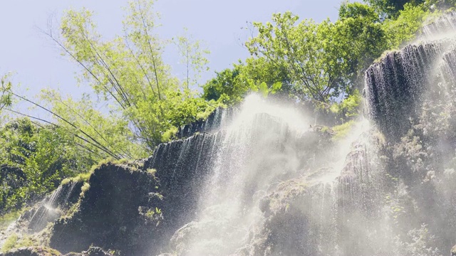 热带森林里的高山瀑布飞溅的水的慢动作。阳光下热带雨林中流动瀑布的底层水流。热带森林中的山河在悬崖上流淌。视频素材