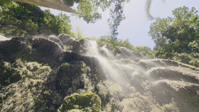 水流在热带森林底部的岩石峭壁上流动。热带雨林中的热带瀑布流水。野生瀑布之间的绿色丛林森林。视频素材