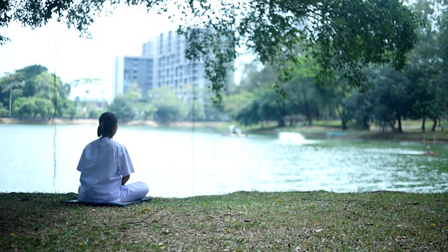 坐在湖边公园草地上的女人。平静和冥想的概念。视频素材