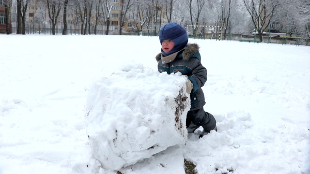 小男孩在操场上为雪人堆了一个大雪球视频素材