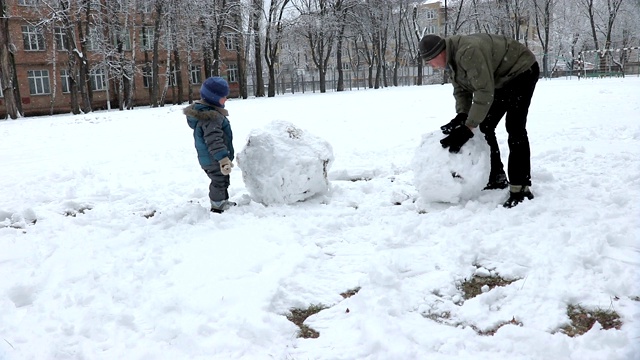 爸爸和小儿子在冬季公园里堆了一个大雪人视频下载