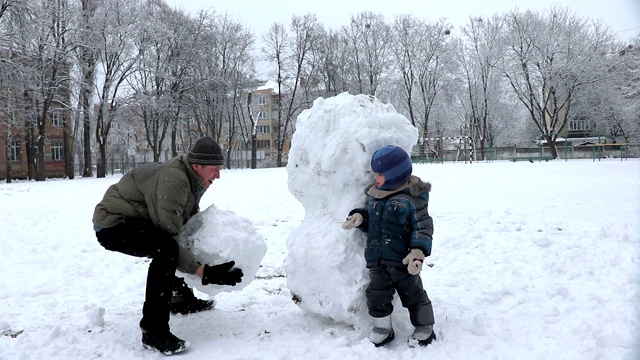 父亲和小儿子在操场上堆了一个大雪人视频素材