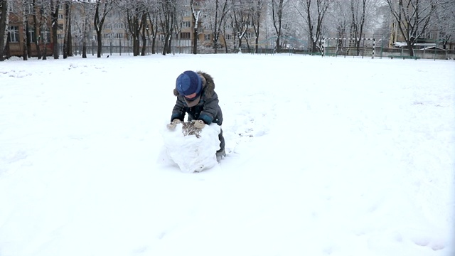 在冬季公园-股票视频中，小男孩为雪人做了一个大雪球视频下载