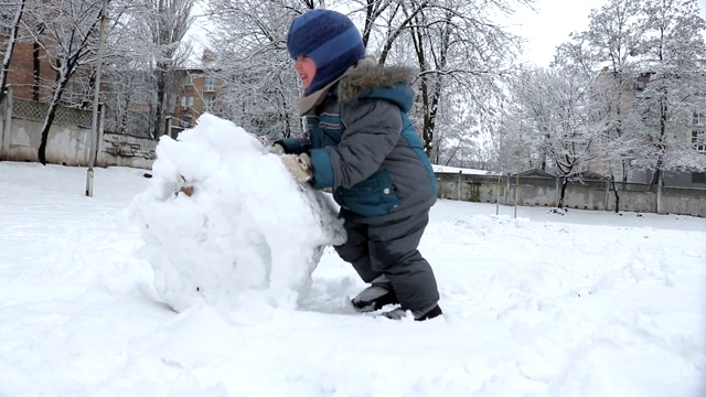 在冬季公园-股票视频中，小男孩为雪人做了一个大雪球视频素材