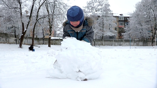 小男孩在操场上为雪人堆了一个大雪球视频下载