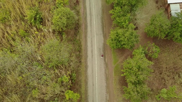 垂直空中在笔直的道路在非洲作为车辆和自行车通过下面视频素材