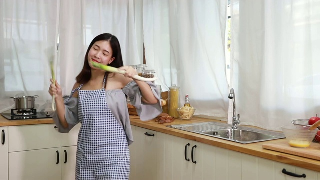 年轻女子一边在厨房做饭，一边又唱又跳。视频素材